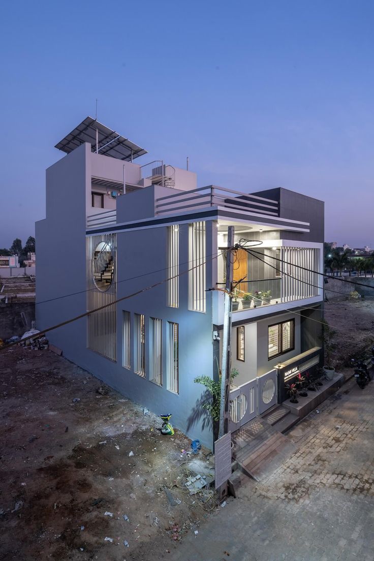 Corner house at dusk with lit balcony, vertical fins and circular stair window